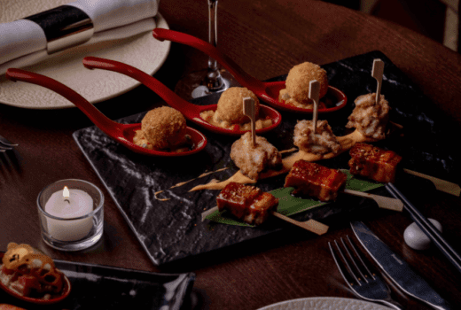 A platter of Asian-inspired appetizers, including crispy bites, skewers, and dumplings, served on a dark slate plate.